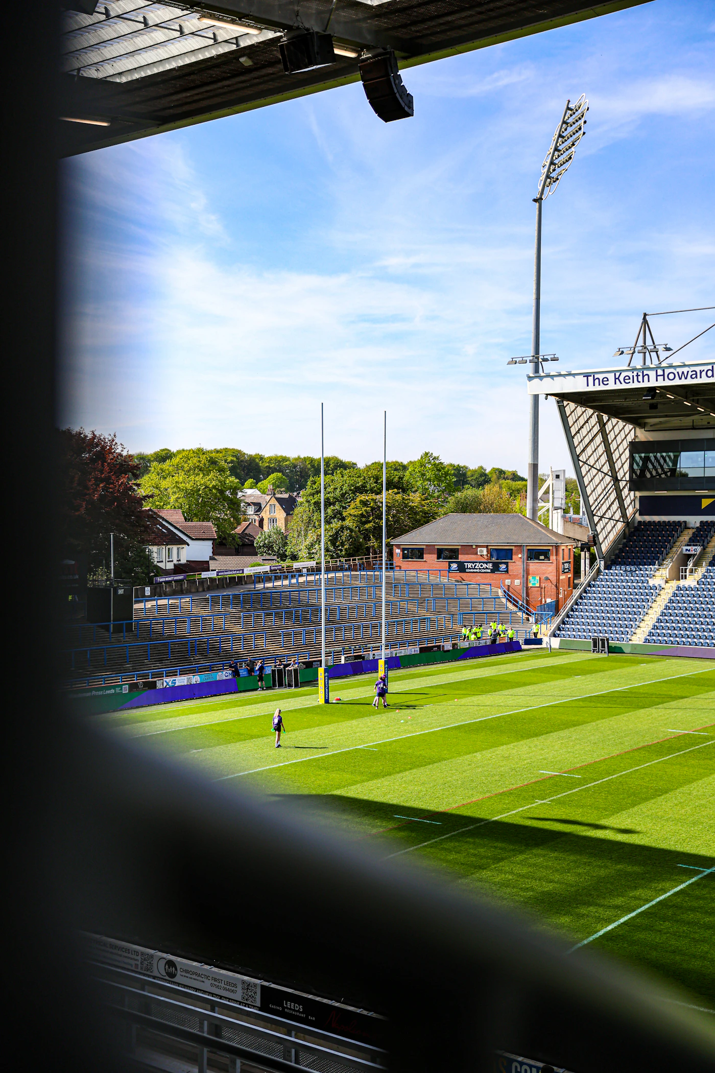 A green rugby field with surrounding stadium stands